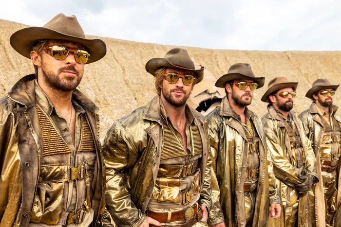 a line up of five idenitcally dressed gold covered "space cowboy" characters, in hats, sunglasses and shiny coats. the two closest to the camera are Ryan Gosling and Aaron Taylor Johnson. The rest are stunt doubles.